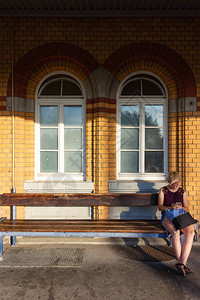 坐在火车站长椅上的年轻女士在巴伐利亚南部烧砖墙前坐背景图片