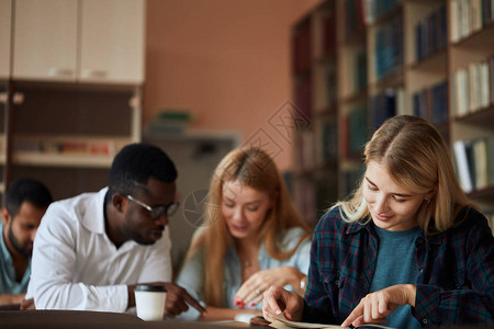 年轻的金发女人和在后台学习的同学一起写笔记学生在大图片