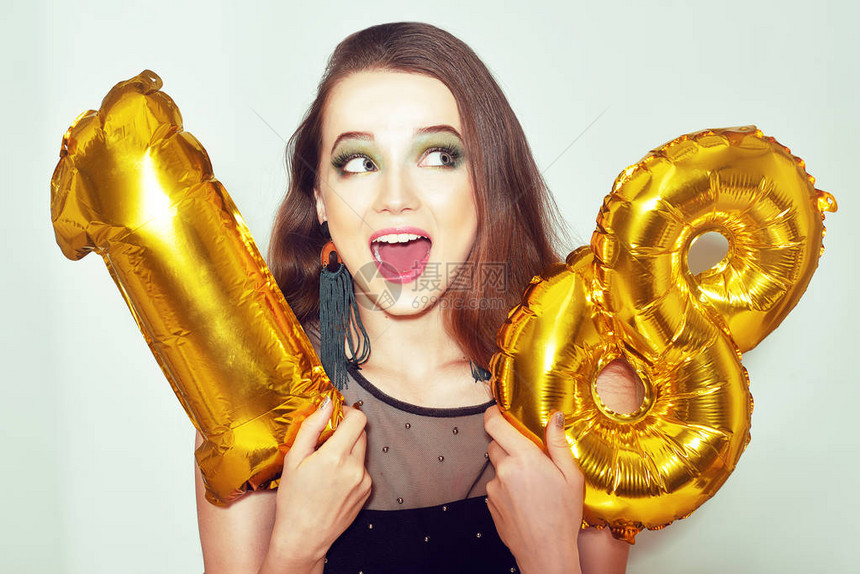 一个18岁生日的女孩带着金色的数字气球兴奋的十八女孩与绿色化妆和黑色礼服微笑模型庆祝和玩乐很可爱的图片