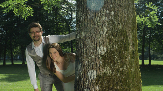 恋爱中的男人和女人在一个令人惊叹的绿色公园中间的树干旁摆姿势新婚夫妇在浪漫婚礼后享受户外照片拍摄年轻夫妇在阳光明媚的花背景图片