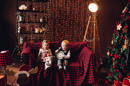 可爱的小男孩和漂亮的金发女孩坐在装饰工作室的长椅上玩圣诞礼物图片