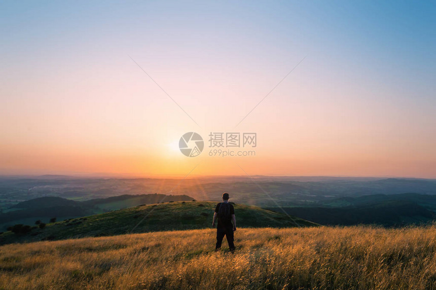 一个山丘上的徒步者看着整个英国风景朝日落的图片