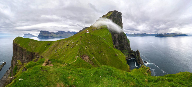 雄伟的岩石悬崖和一座白色的小灯塔建在陡峭的草山上图片