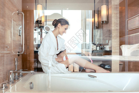 女人通过在坐浴缸上的旅馆浴室刮腿毛来理发图片