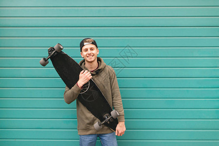 穿着散装的快乐溜冰者手持长板站在绿的明墙背景之下图片