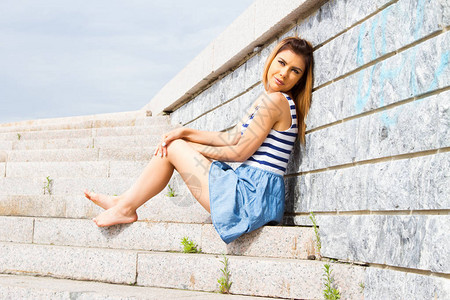 女孩坐在水泥楼梯的阶梯上靠在石墙图片