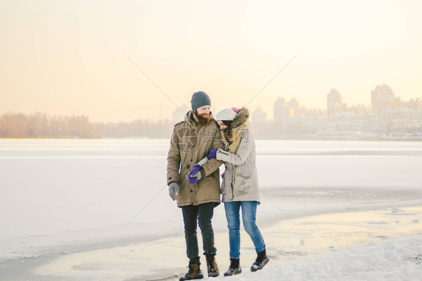 主题圣诞假期冬季新年轻时尚的高加索情侣异恋在结冰的湖岸上行走日期在日落的冬天的情人节爱图片