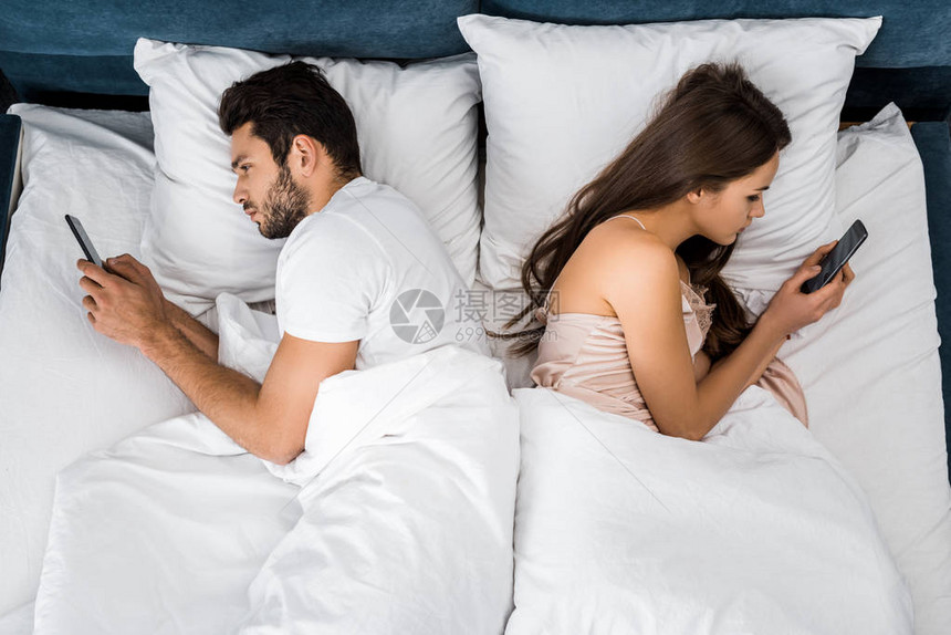 早上躺在床上使用智能手机的年轻夫妇图片