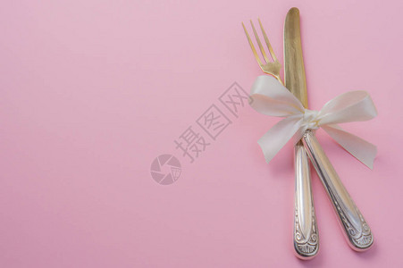 银色刀叉白色缎面蝴蝶结粉红色背景图片