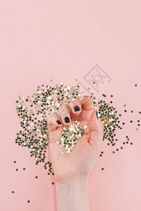 新年或圣诞节女手黑色修指甲的顶部视图覆盖着金色星纸屑图片