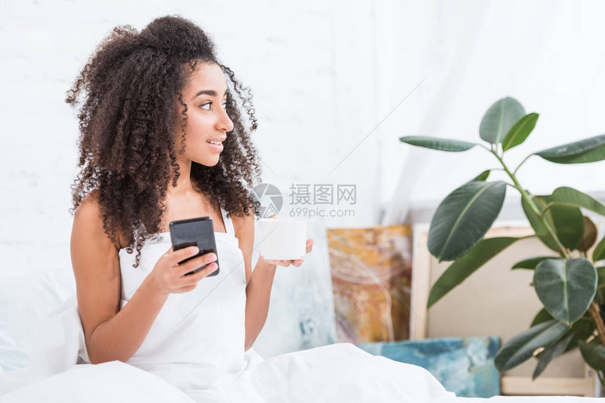 非洲裔美国年轻女子早上在家时在床上用智能手图片