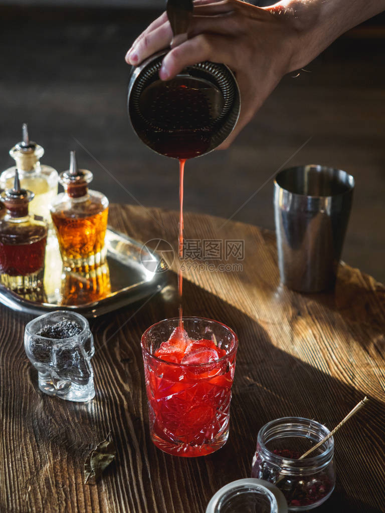 酒保在酒吧里做红鸡尾酒在玻璃杯里倒鸡尾图片