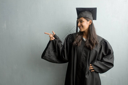 年轻毕业的印度女青年站在一面墙对面背景图片