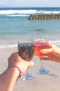 两只手握着杯子和红酒在海面背景上男女手拿着图片
