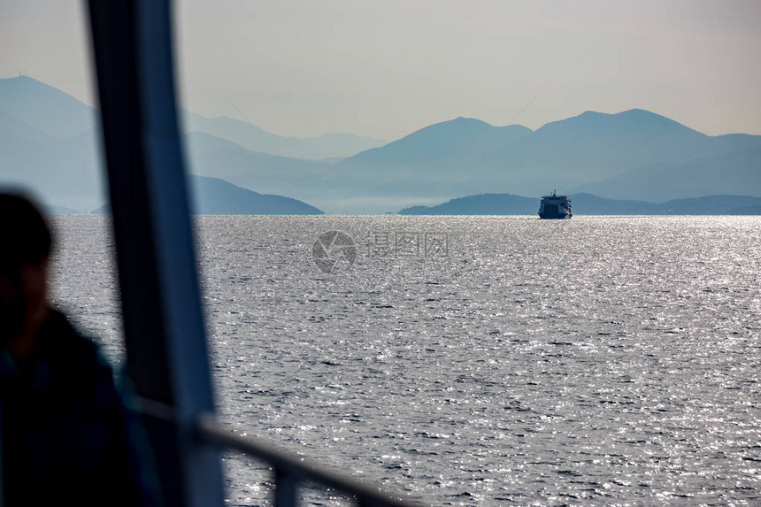 希腊远处的渡船阳光明媚的冬季海景部分无法辨认的男模糊亮色双影带美丽的蓝水光反射旅行冷图片