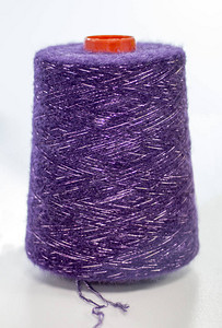 在白色背景的线轴上带有卢勒克斯的紫色纱线图片