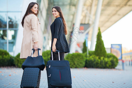 度假两个快乐的女孩一起出国旅行在机场携带手提箱行李图片