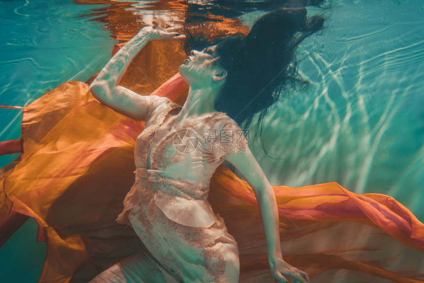 穿着橙色裙子的女孩是梦幻和冥想漂浮在水下就像转世图片