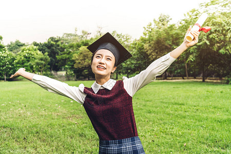 在大学公园毕业的学生年轻女子和学士礼服获得成功庆祝毕图片