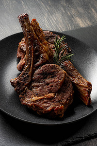 木制背景上黑盘上的新鲜熟烤牛肉排骨图片