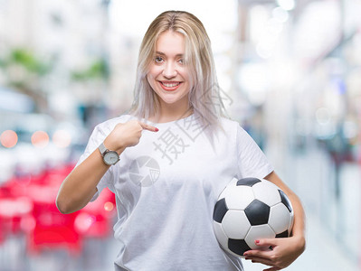 年轻的金发女子在孤立的背景下拿着足球图片
