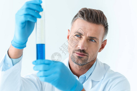 英俊科学家有选择焦点看着用蓝色试剂在白色上图片