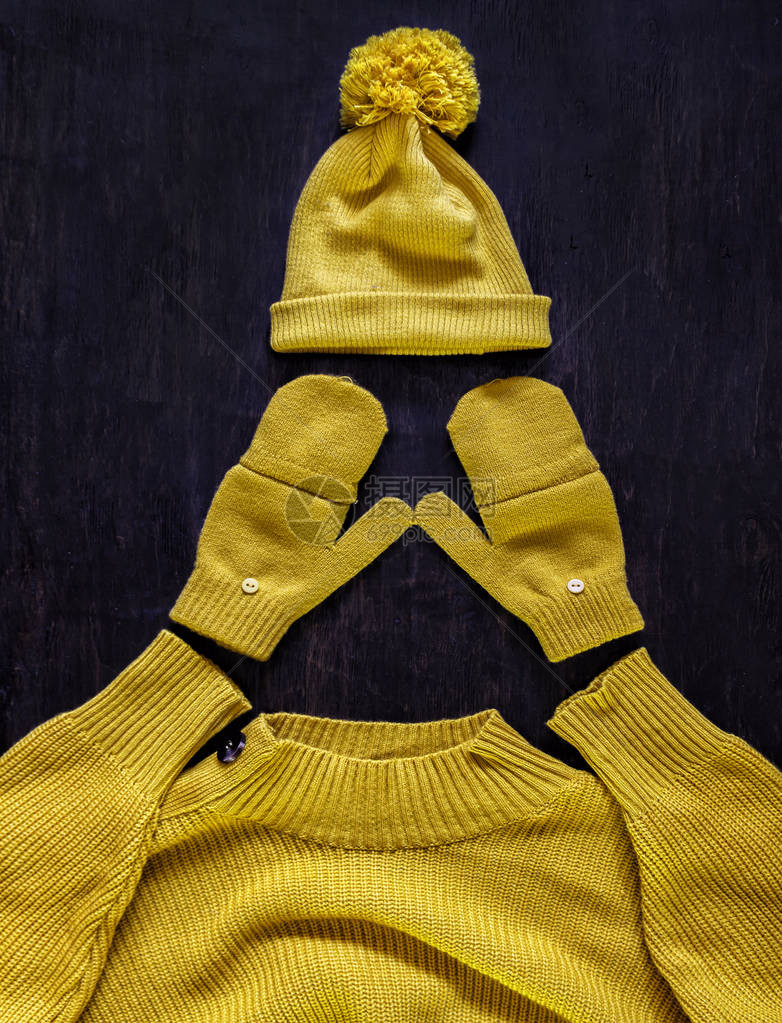 深色木质背景上带绒球手套黄橙色毛衣的帽子图片