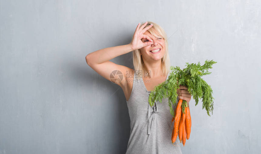 高加索成年女在灰色的格朗基墙上拿着新鲜的胡萝卜图片