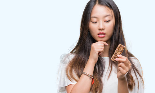 年轻的亚洲女在与世隔绝的背景下吃巧克力能量棒图片