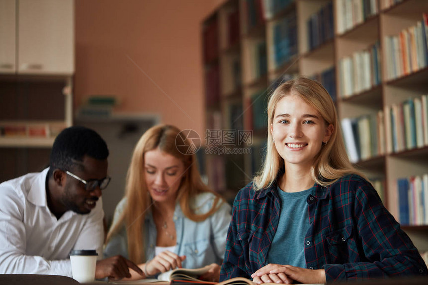 微笑迷人的金发女孩在大学图书馆读书时做一些笔记图片