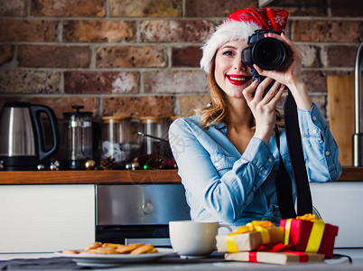 美丽的年轻摄影师坐在厨房里拿着相机和礼物图片