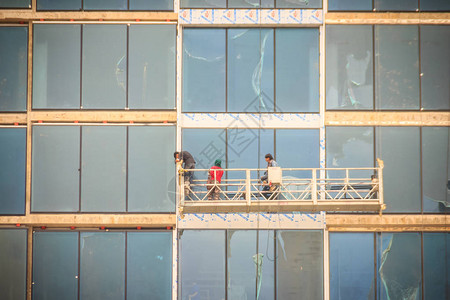 建筑工人在摩天大楼玻璃幕墙的悬挂式摇篮平台上图片