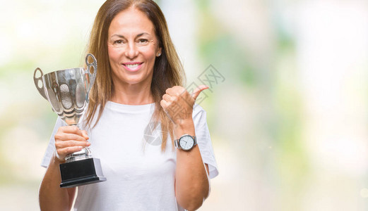 中年西班牙裔获奖者庆祝奖项的女在孤立的背景下举起奖杯图片