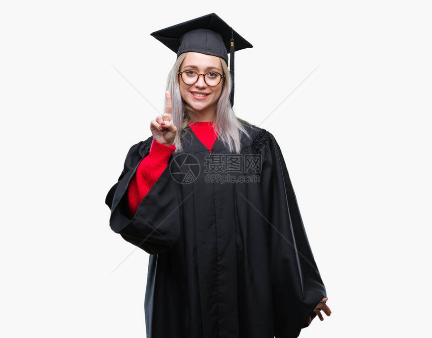 身穿毕业制服的金发年轻女郎在孤立的背景展出和指着一号手指时微笑着自信图片