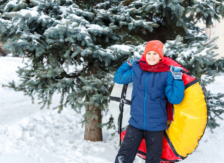 戴着帽子红围巾和蓝色夹克的开朗可爱的小男孩在雪地上拿着管子图片