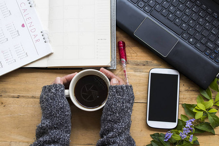 手机日历商务电脑和女手持热咖啡的手在冬季在办公桌的图片