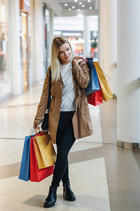 身穿棕色外套红色蓝色黄色购物袋的金发小女孩留在大城市购物中心图片