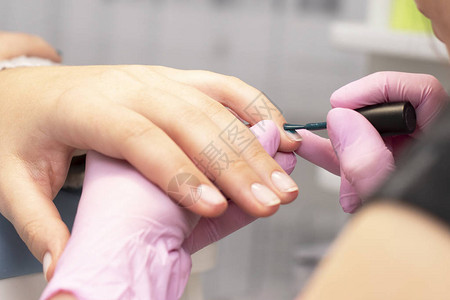 在美甲沙龙一名粉色手套修指甲师用绿钉子覆盖客户的指甲图片