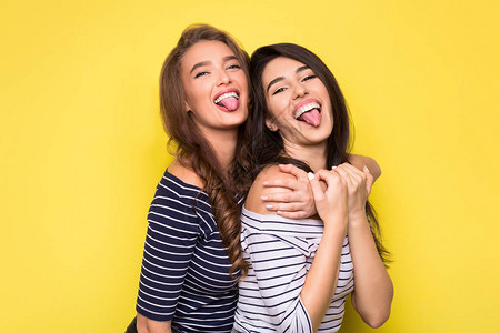 两位美女拥抱的生活方式肖像和黄色背景的舌头露出双漂亮女人图片