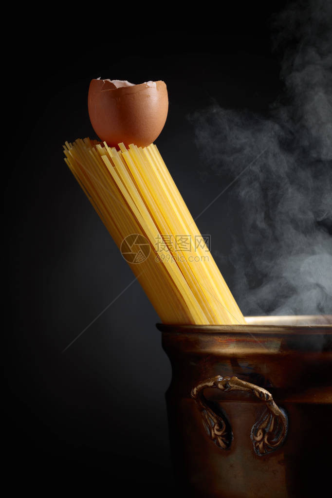 Raw意大利面条和鸡蛋装在旧黄铜锅里黑色背图片