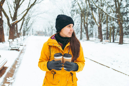 妇女带着咖啡杯走在雪地城市公园温暖寒图片