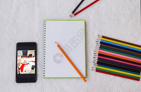 笔记本彩色绘画用铅笔和带雪人照片的电话图片