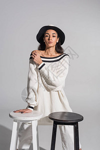 穿着时髦的白色衣服和帽子的漂亮非洲裔美国女孩站在黑白椅子旁背景图片