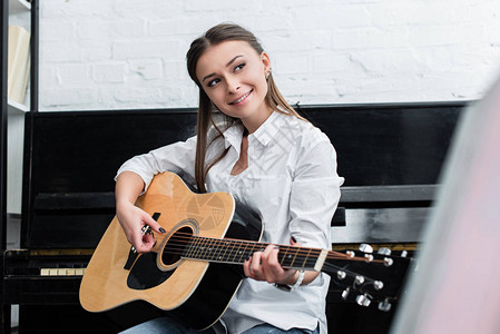 微笑的女孩坐在客厅里弹吉他在背景上用图片