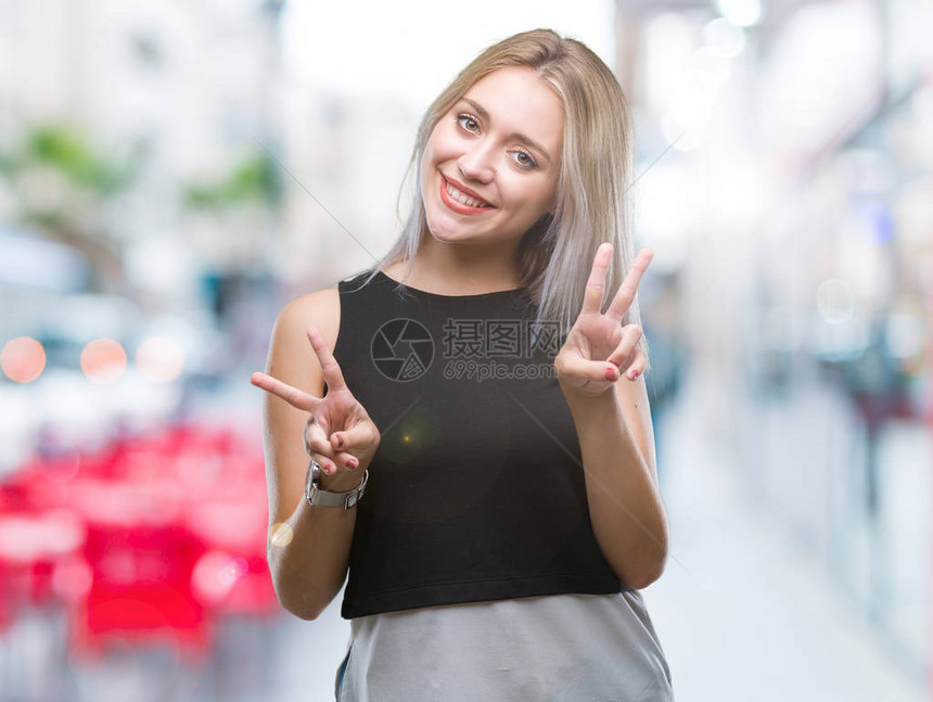 身处孤立背景的金发年轻女子微笑着看摄影机显示手指在做胜图片