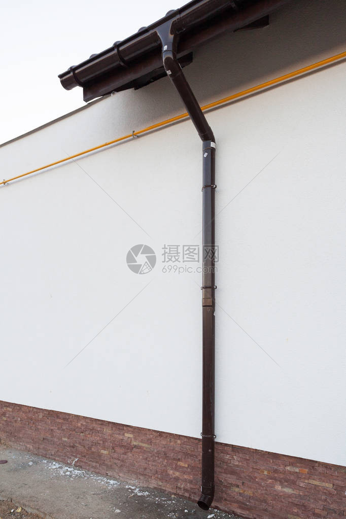 新舒适屋白墙上棕色雨水槽管的垂直照片图片