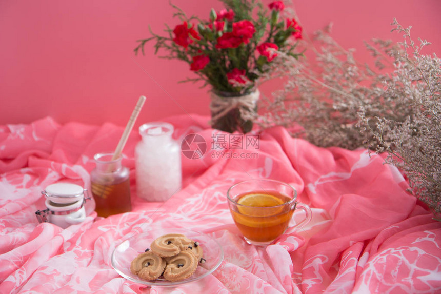 在透明杯子里的柠檬茶与香草饼干在碟盘上配有糖方块和蜂蜜在杯中粉红色的音调和图片