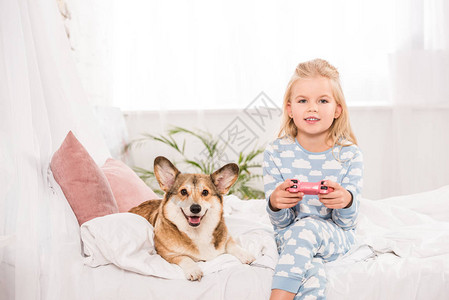 孩子坐在床上与PembrokewelshCorgi狗图片