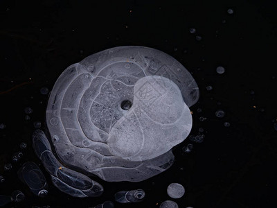 投掷的石头从湖冰下的气泡中创造出惊人的形状一个小湖的冰洞图片
