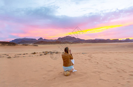 女旅游摄影师在约旦沙漠中拍摄美丽的日落黄昏景色的背影图片